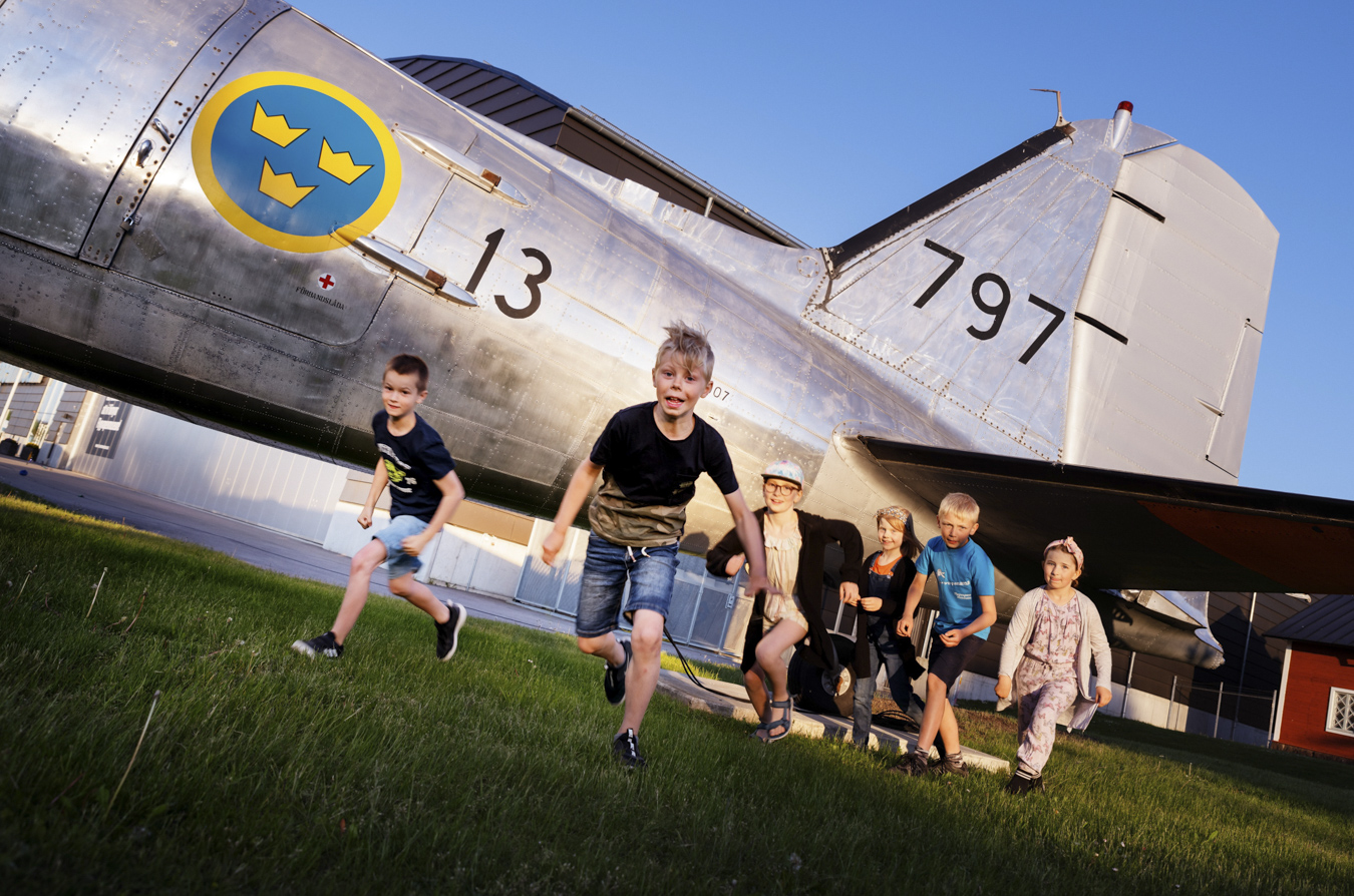 flera barn som springer mot kameran framför ett gammalt stridsflygplan.