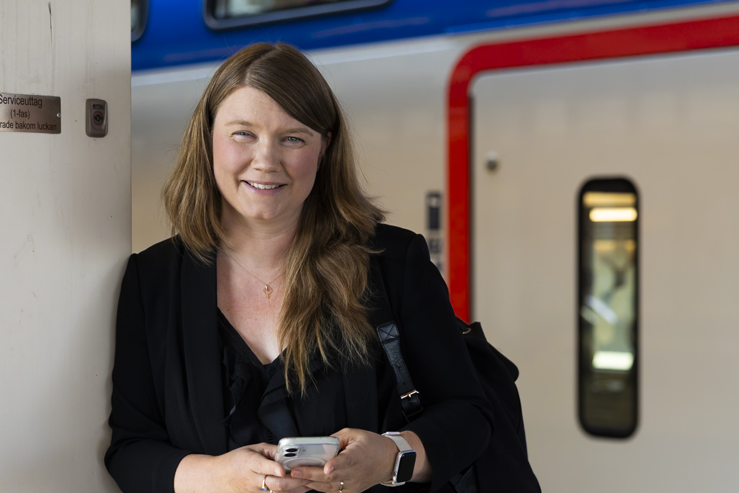Kvinna som står med mobiltelefon utanför ett mälartåg