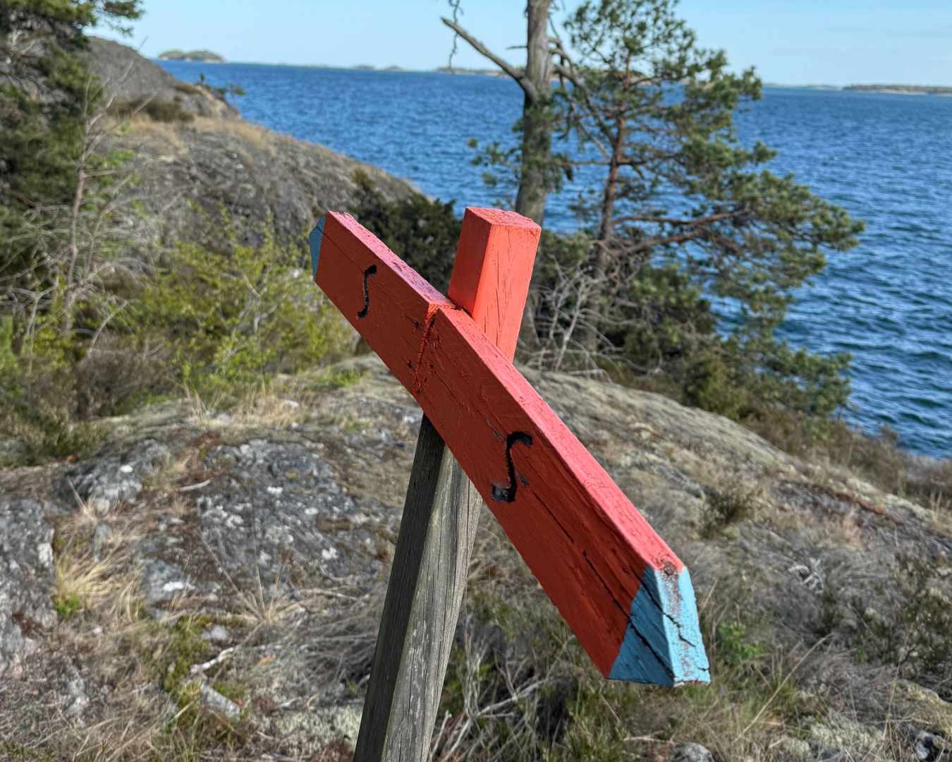 röd träskylt med pilar för markering av vandringsled vid vattnet