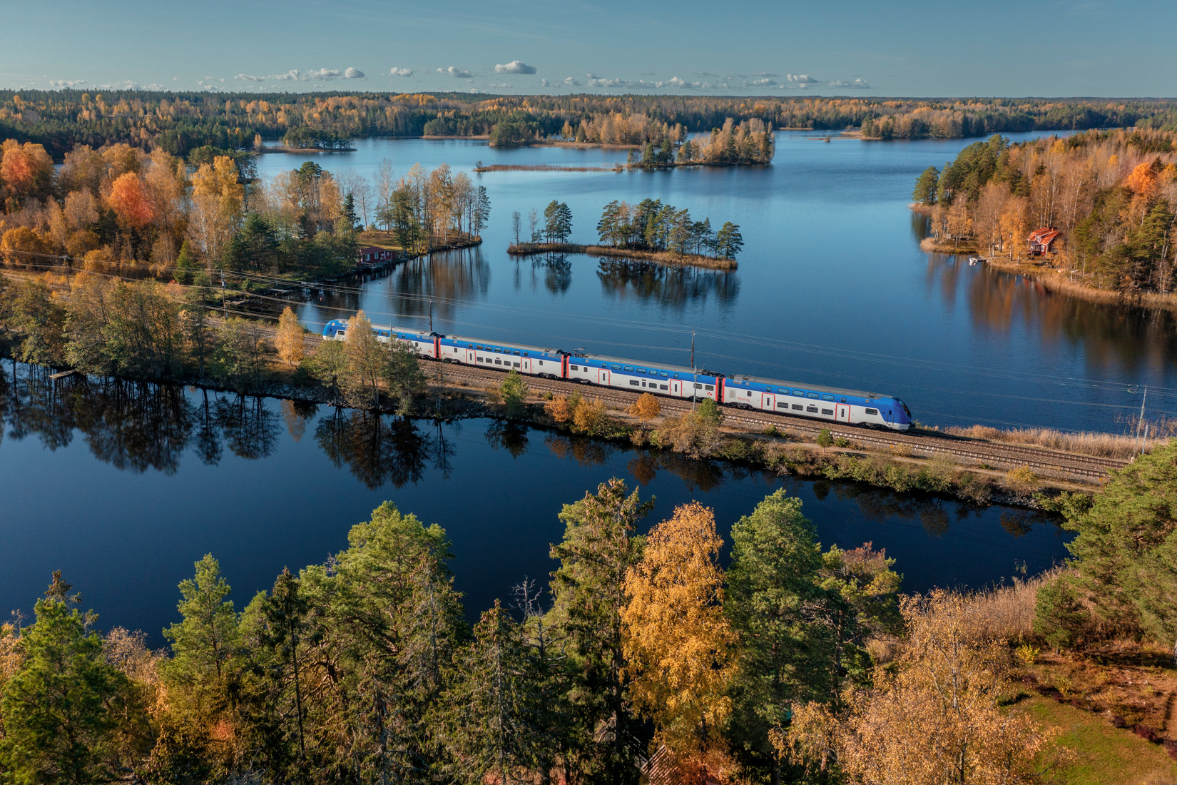 ett mälartåg som åker längs spåret med vatten på båda sidor och träd i höstfärger