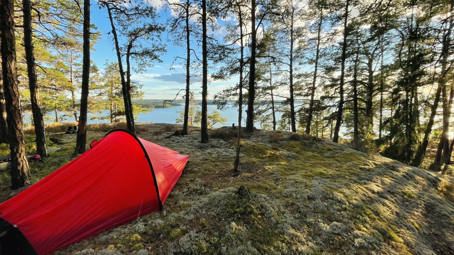Ett rött tält på en bergsknall i skogen med utsikt över vattnet