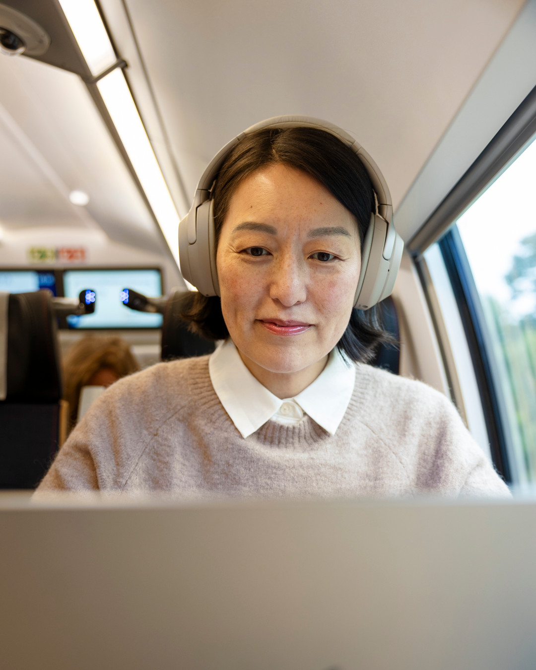 En kvinna med hörlurar på sig medan hon använder en bärbar dator.